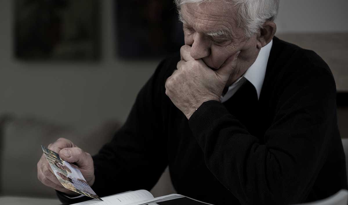 Lonely elderly senior looking at family photo feeling isolated